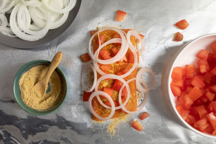 Sprinkle seasoning and top it with onion rings and tomatoes