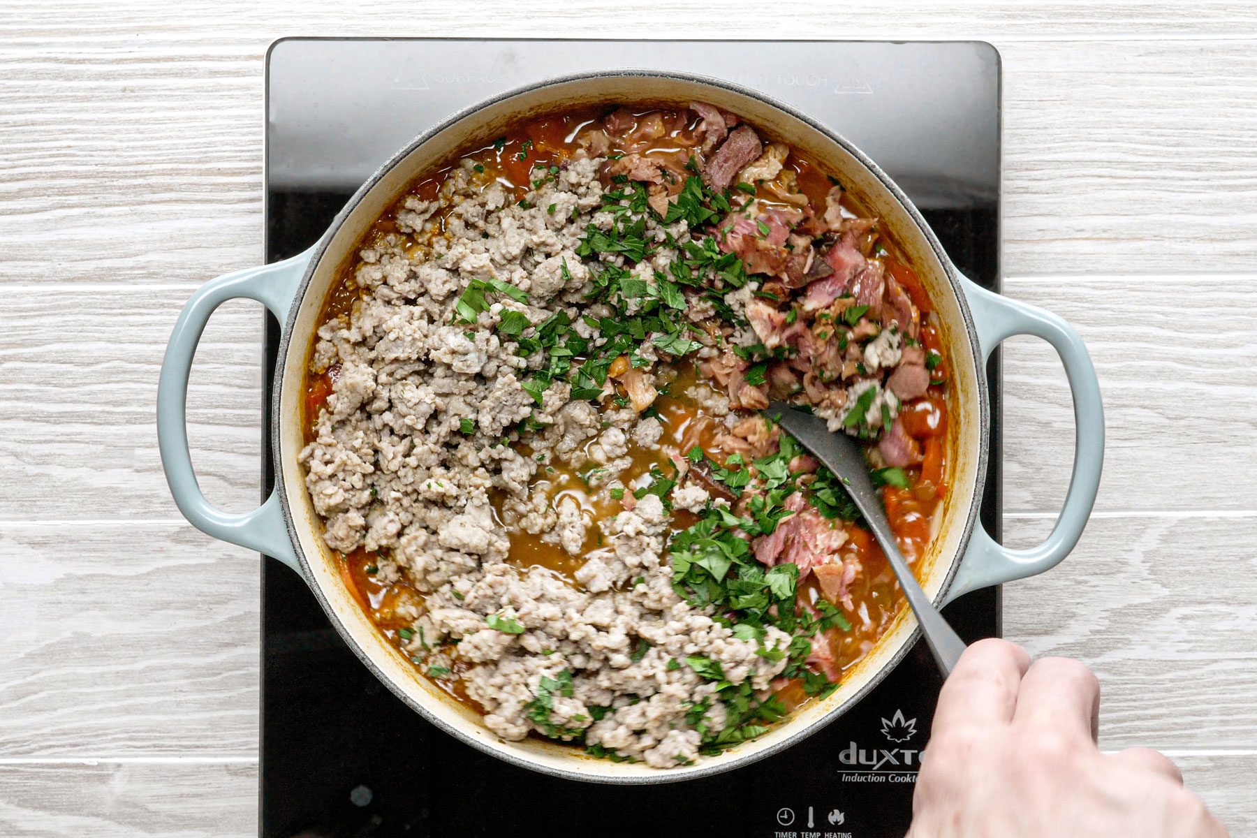 Mixing the Ham And Lentil Soup with a wooden spatula in a large dutch oven 