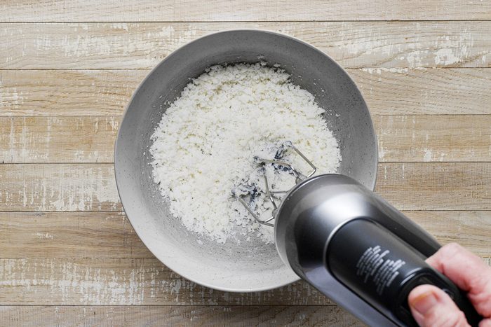 A hand holding a blender to a bowl of sugar and butter mixture.