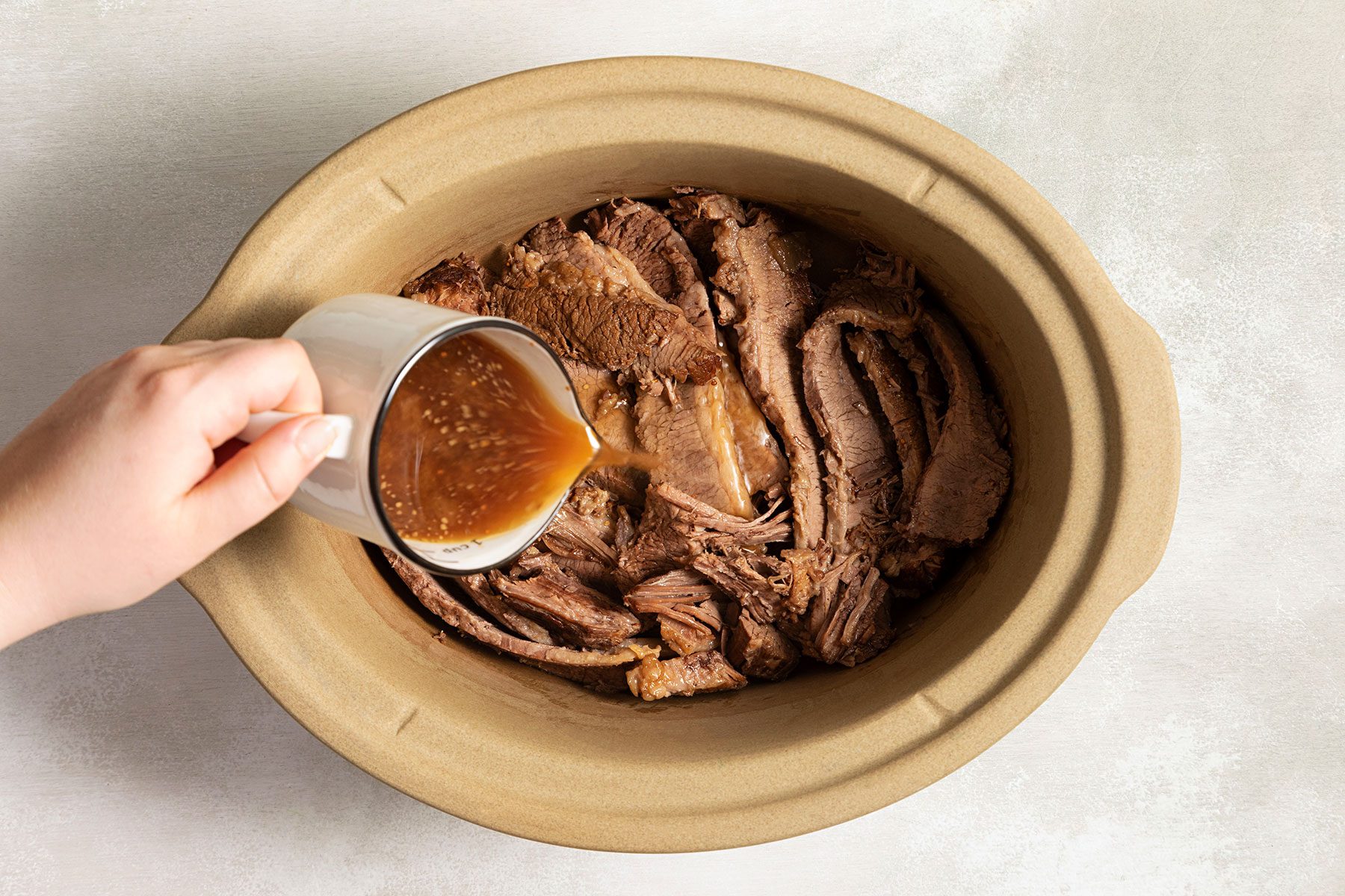 Pouring juices over brisket in slow cooker