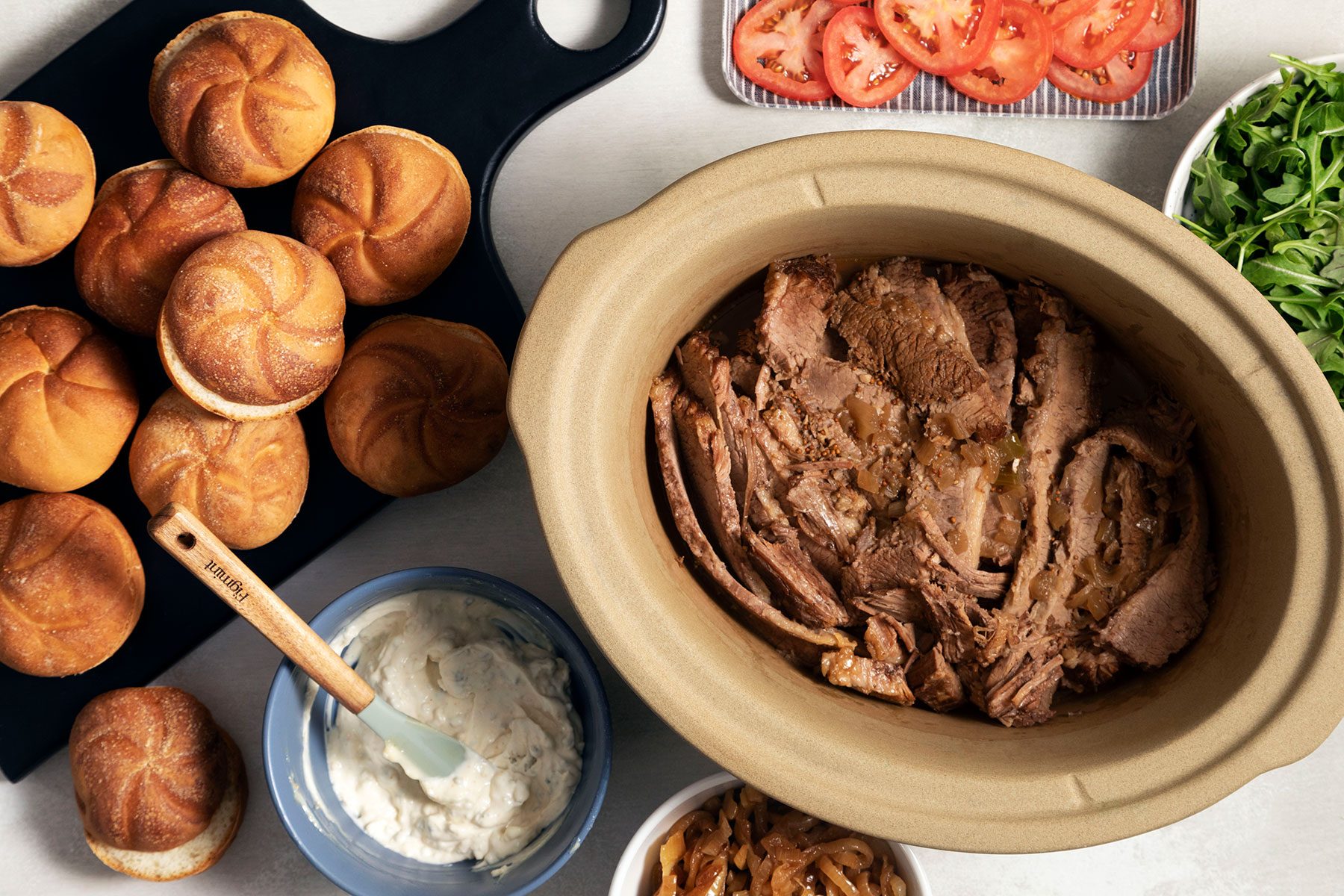 Brisket in slow cooker with buns, dip and sliced tomatoes on the side