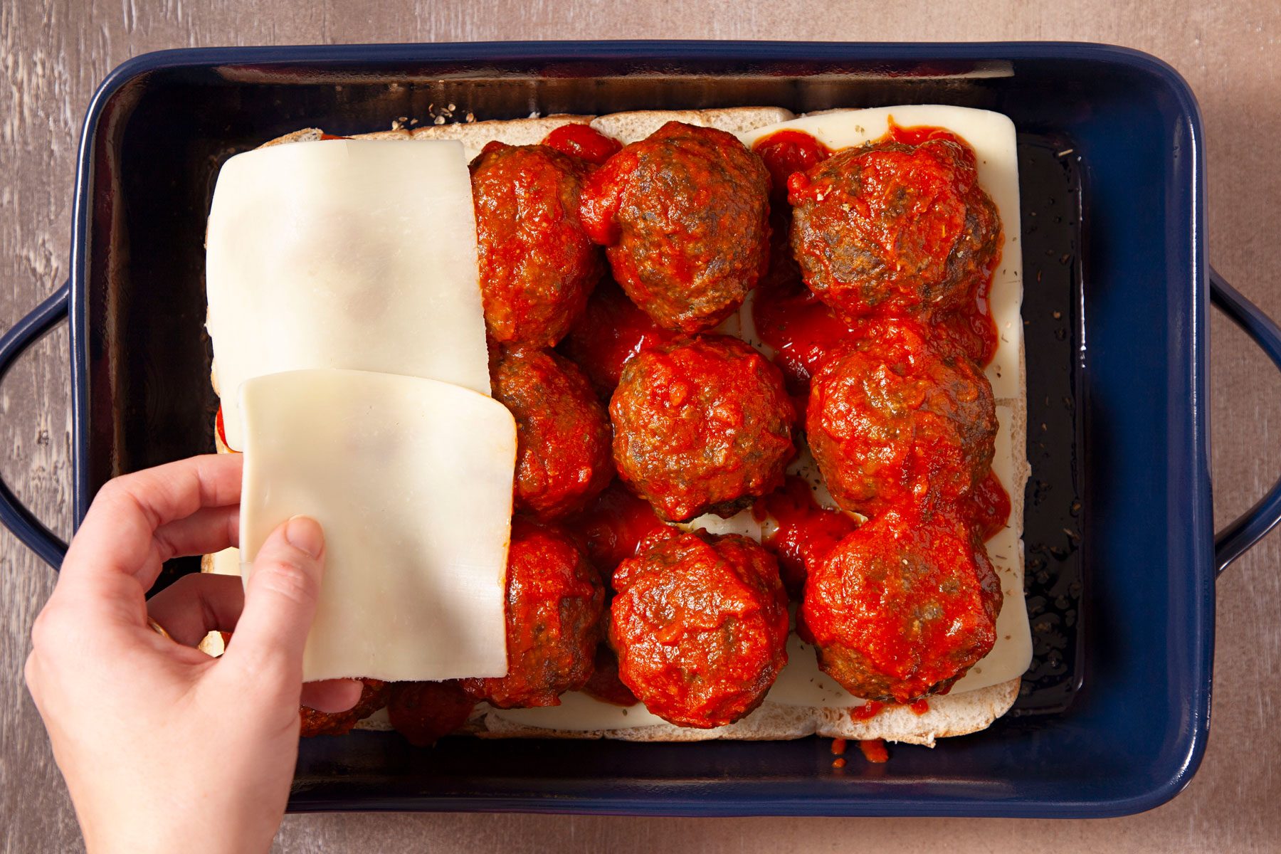 Pullting cheese slices on meat balls on a baking tray