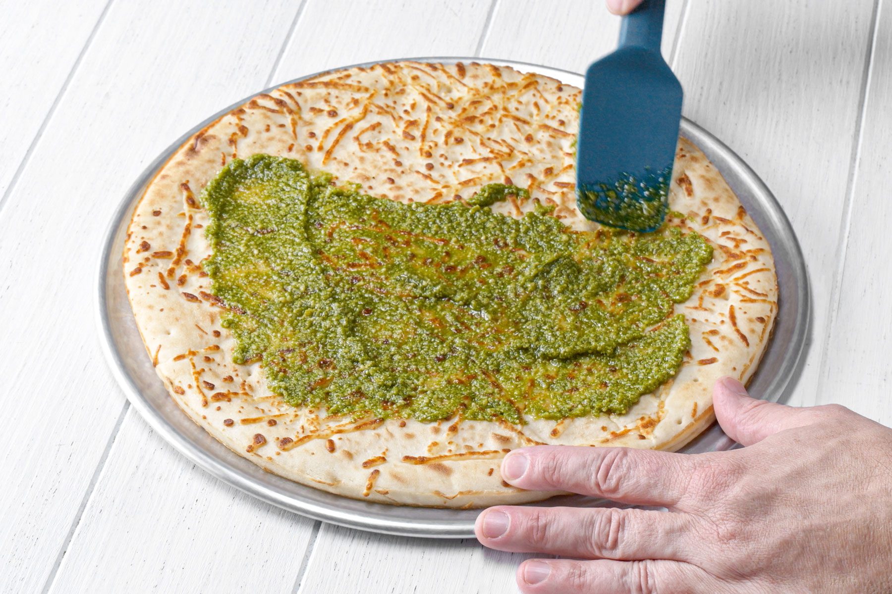 Spreading pesto on pizza crust with spatula