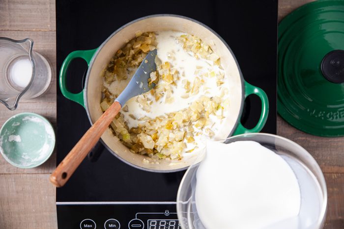 Pouring milk in onions and garlic in a saucepan