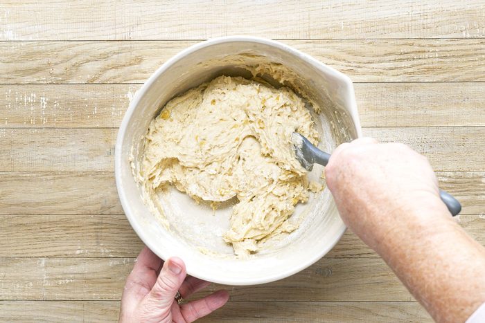 a person folding Chocolate Chip Banana Bread Batter in a large bowl on a wooden surface