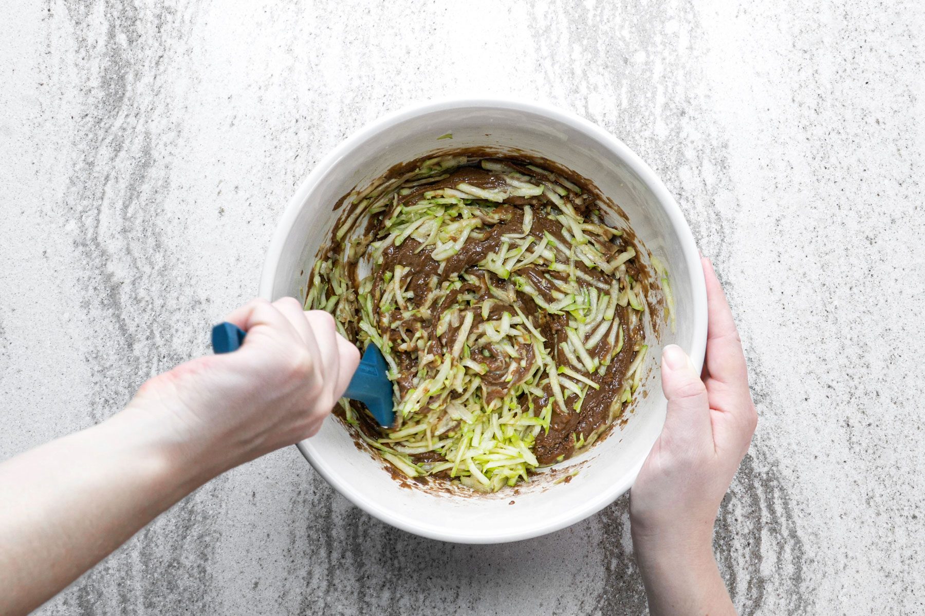 Folding the shredded zucchini into the flour batter with a spatula.
