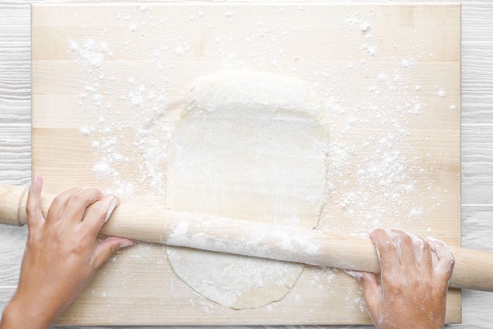 A person rolling the dough ightly floured surface