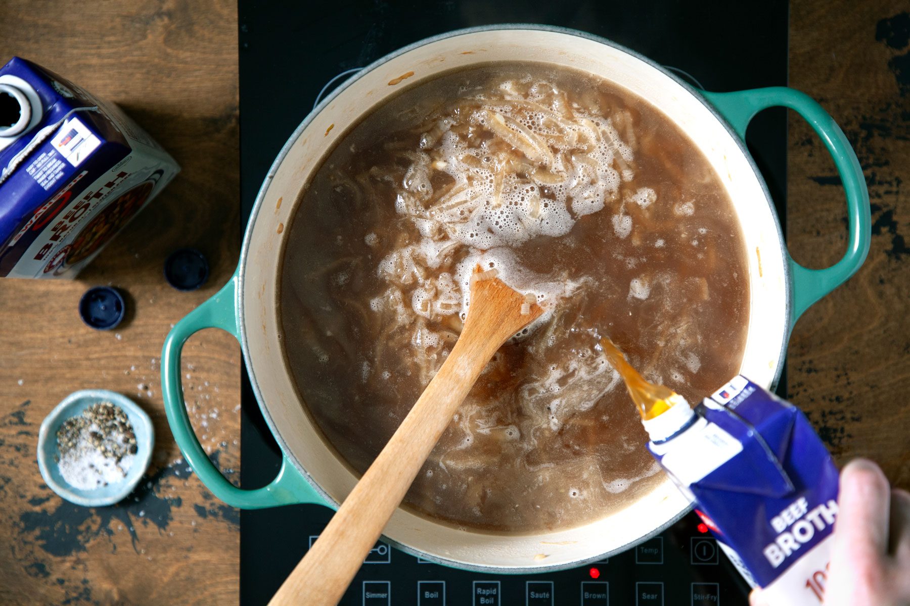 Adding the broth in the onion soup being cooked in a dutch oven.