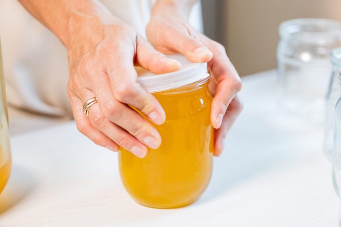 Woman's hands close the lid of a jar of honey standing on a white table and next to a saucer with a spoon