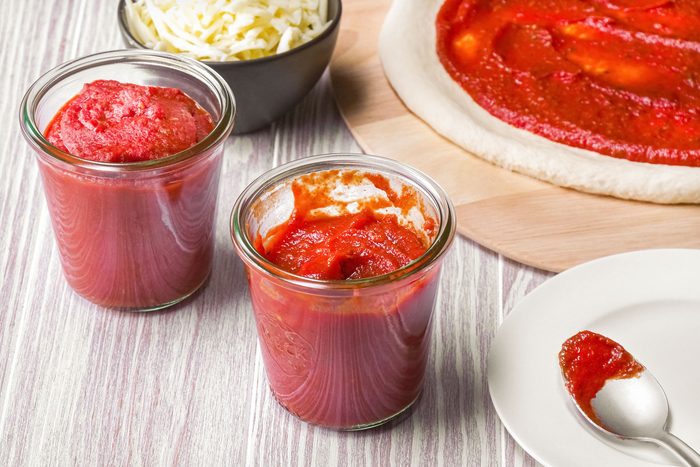 on a wooden surface Homemade pizza sauce in round glass containers and a bowl of cheese next to it