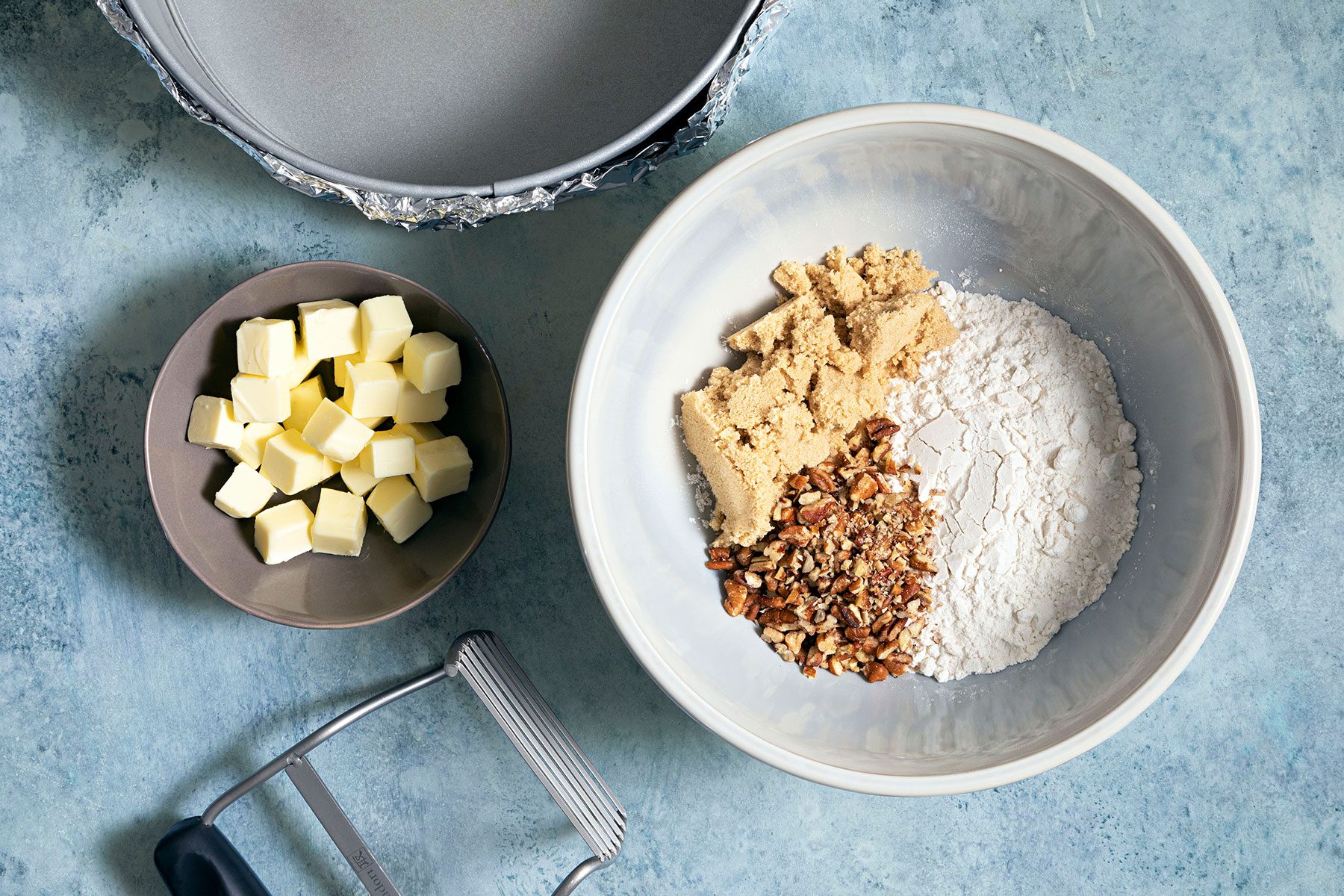 Brown sugar, pecans and flour in bowl with cubes of butter in a smaller bowl on side