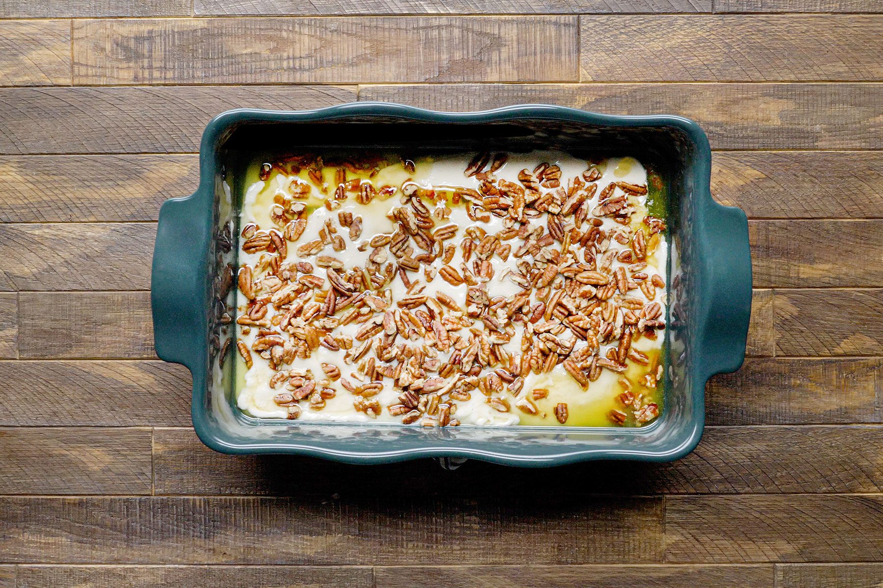 Pecans layers over batter in blue baking tray