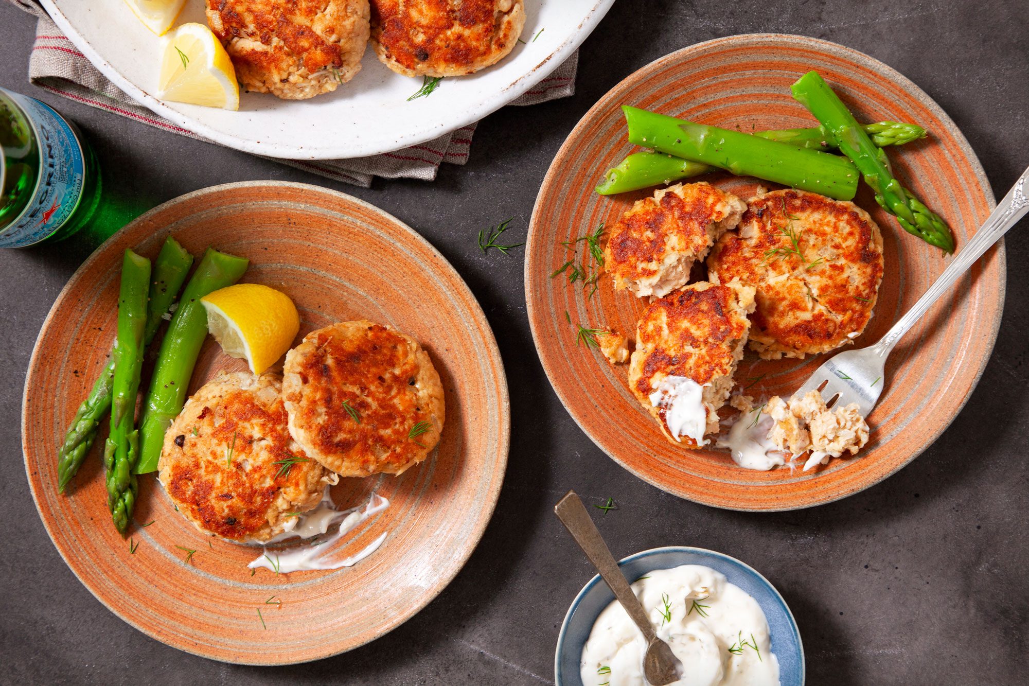 Salmon Patties Served on Two Small Plates with Lemon Wedges and Some Steamed Greens