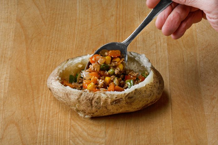 Adding meat mixture into each potato shell with a spoon