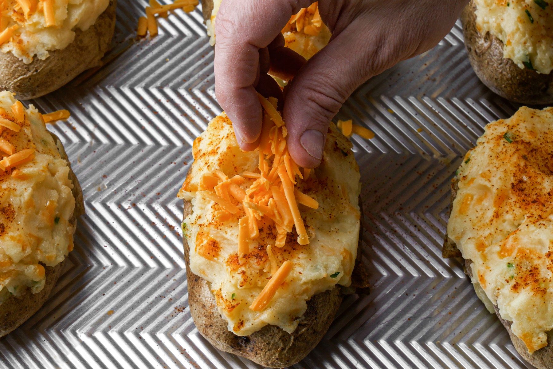 Sprinkling potatoes with cheese on a baking dish