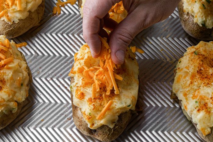 Sprinkling potatoes with cheese on a baking dish