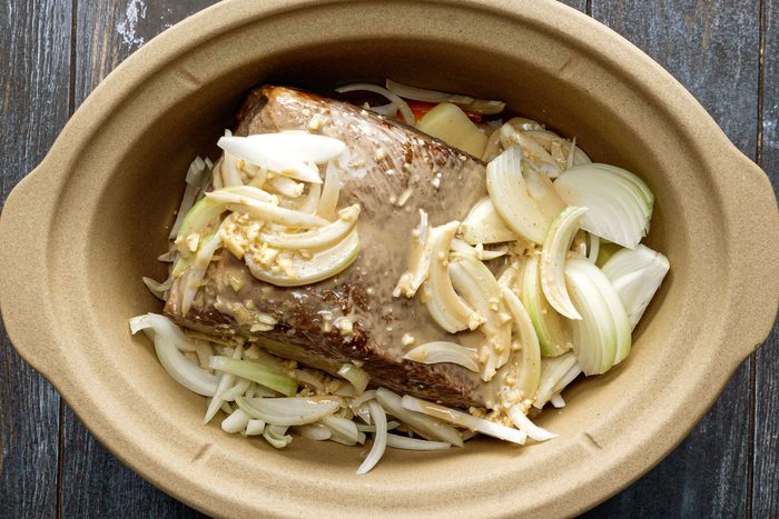 Onions, Rump Roast, Carrots and Potatoes in a Slow Cooker on a Wooden Surface