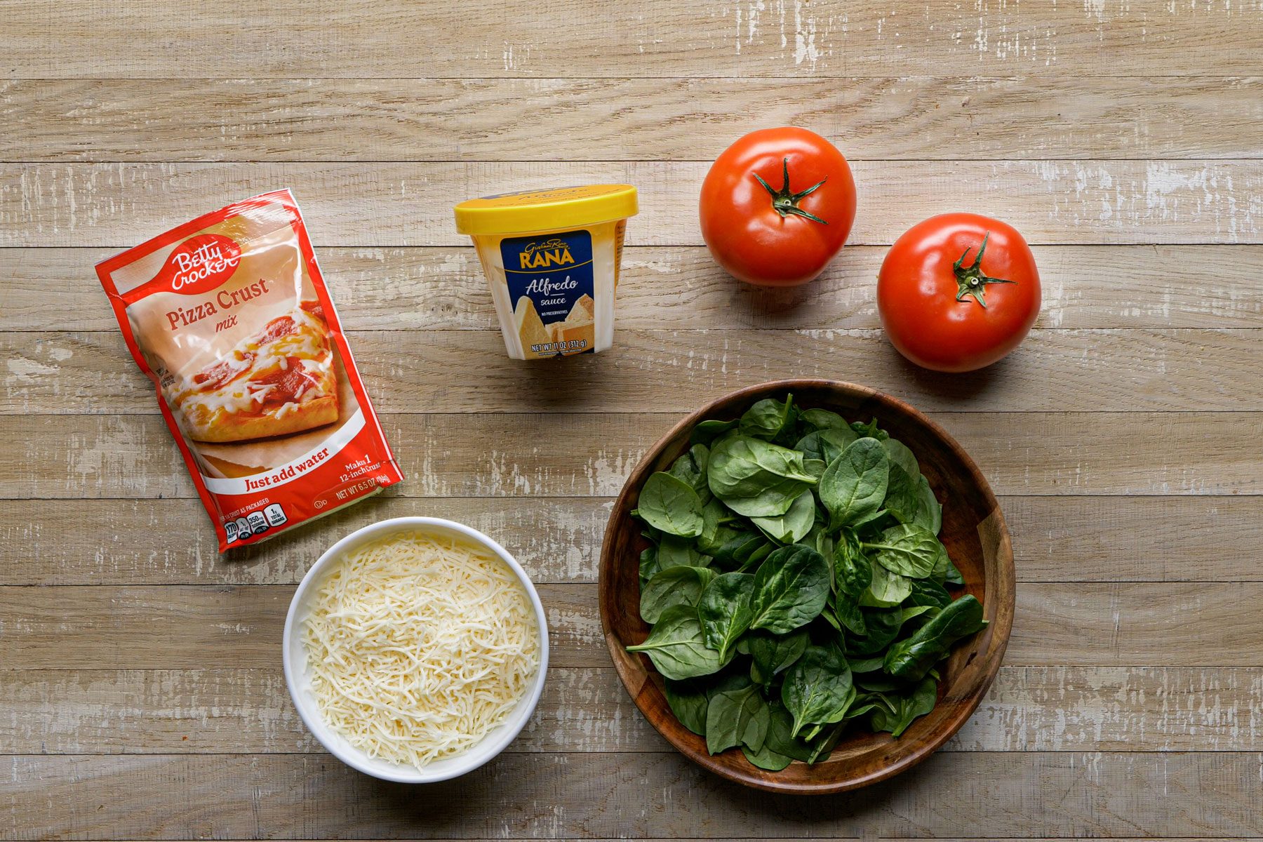 Pizza crust spinach cheese and other ingredients on a wooden table