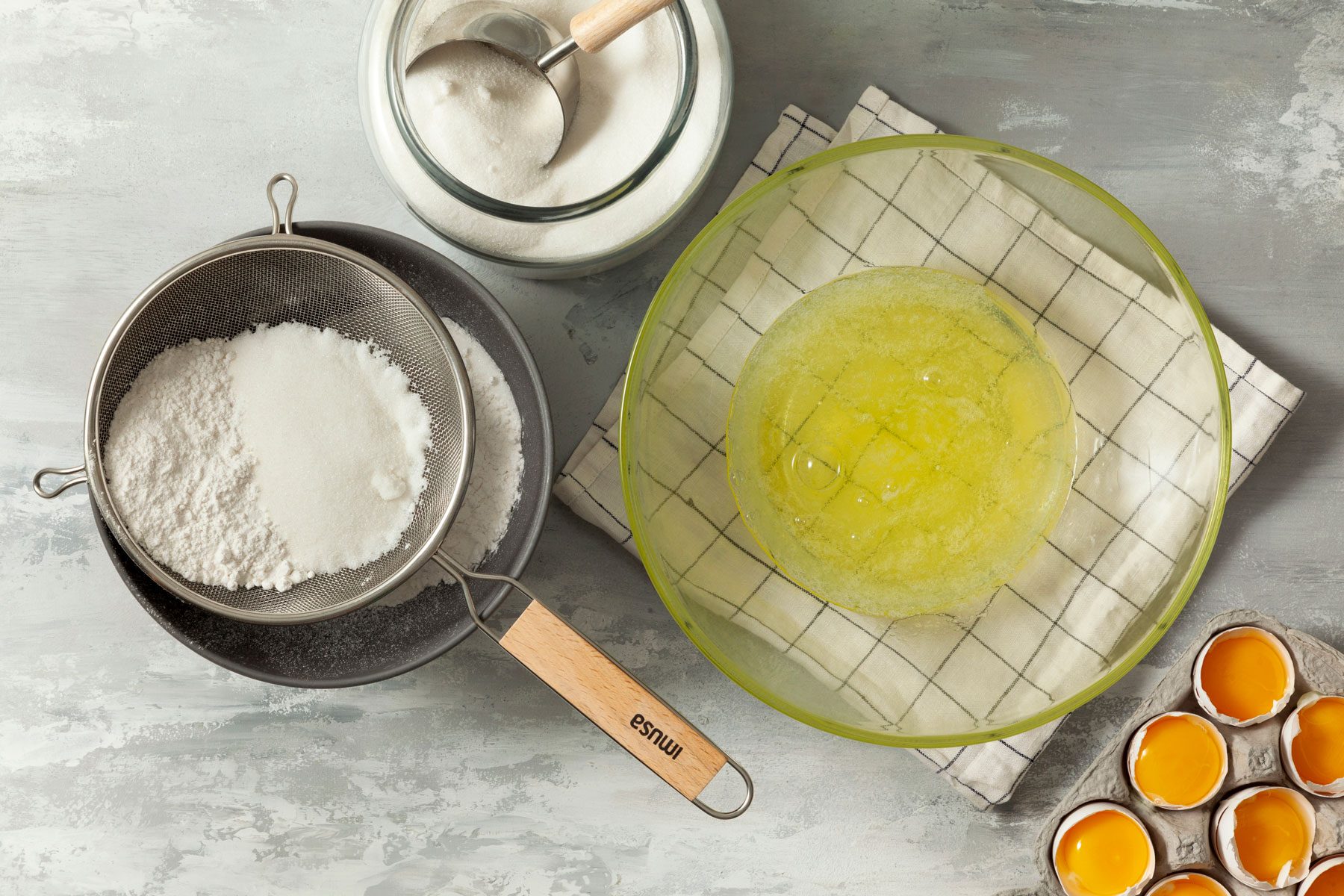 Egg whites in a large bowl and flour in another bowl on a marble countertop 