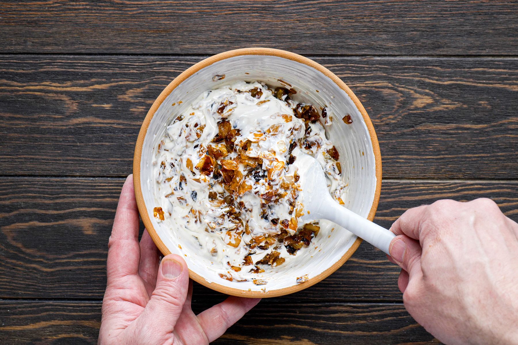 Stirring together cream and onions using a spatula in a small bowl