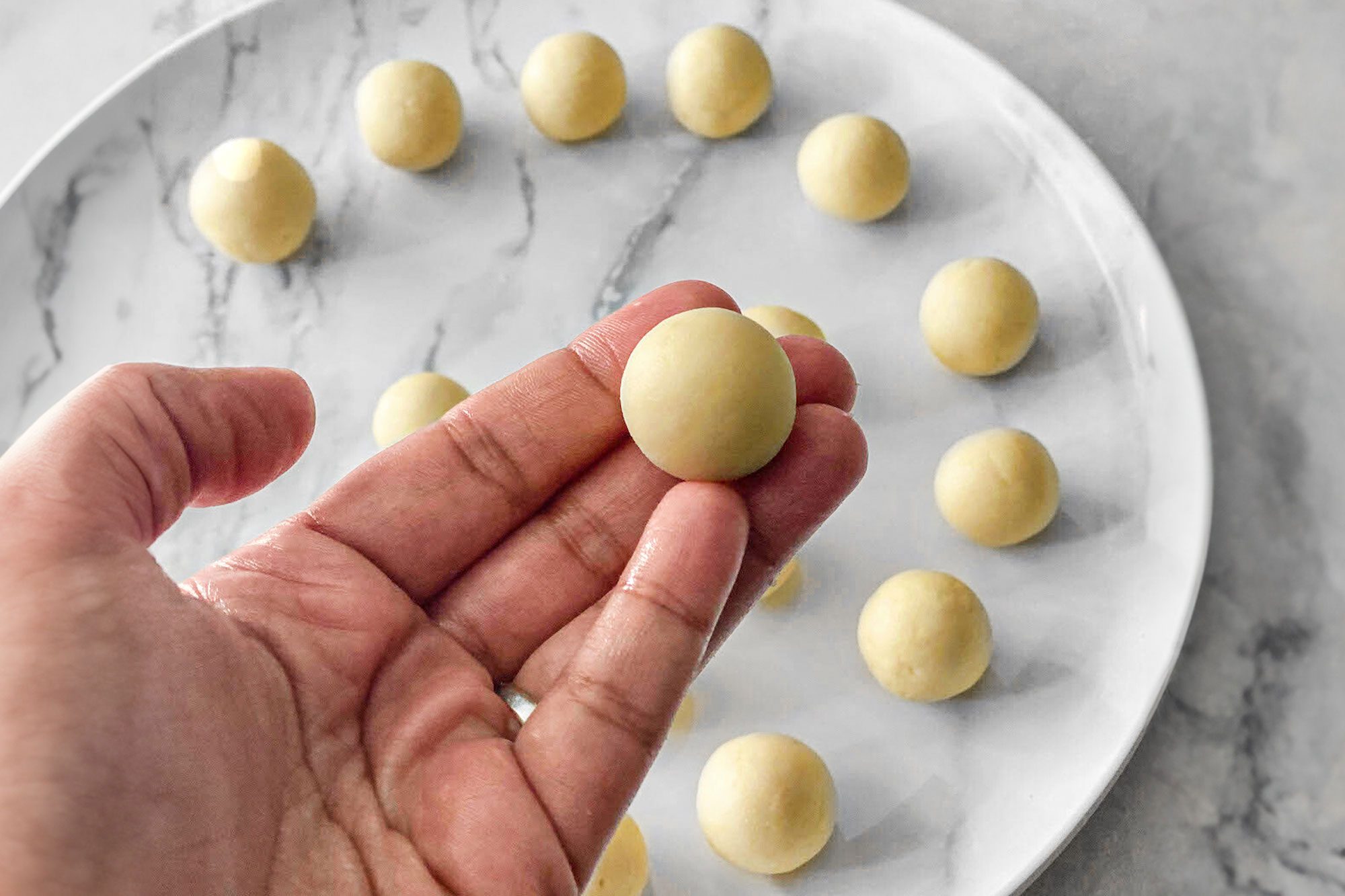 raw gulab jamun in a hand and a lot of gulab jamun placed on a plate in the background