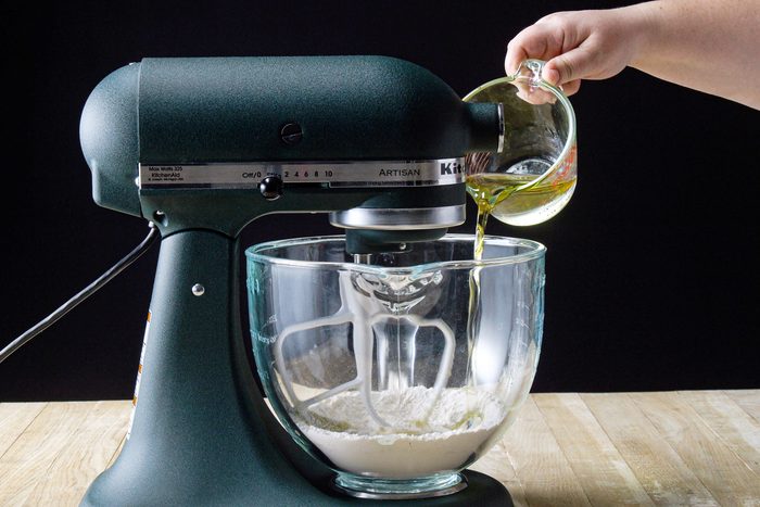 A hand pouring liquid into a bowl of flour