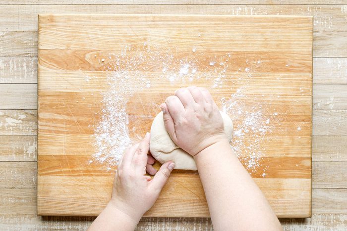 A person's hands kneading dough on a wooden surface.