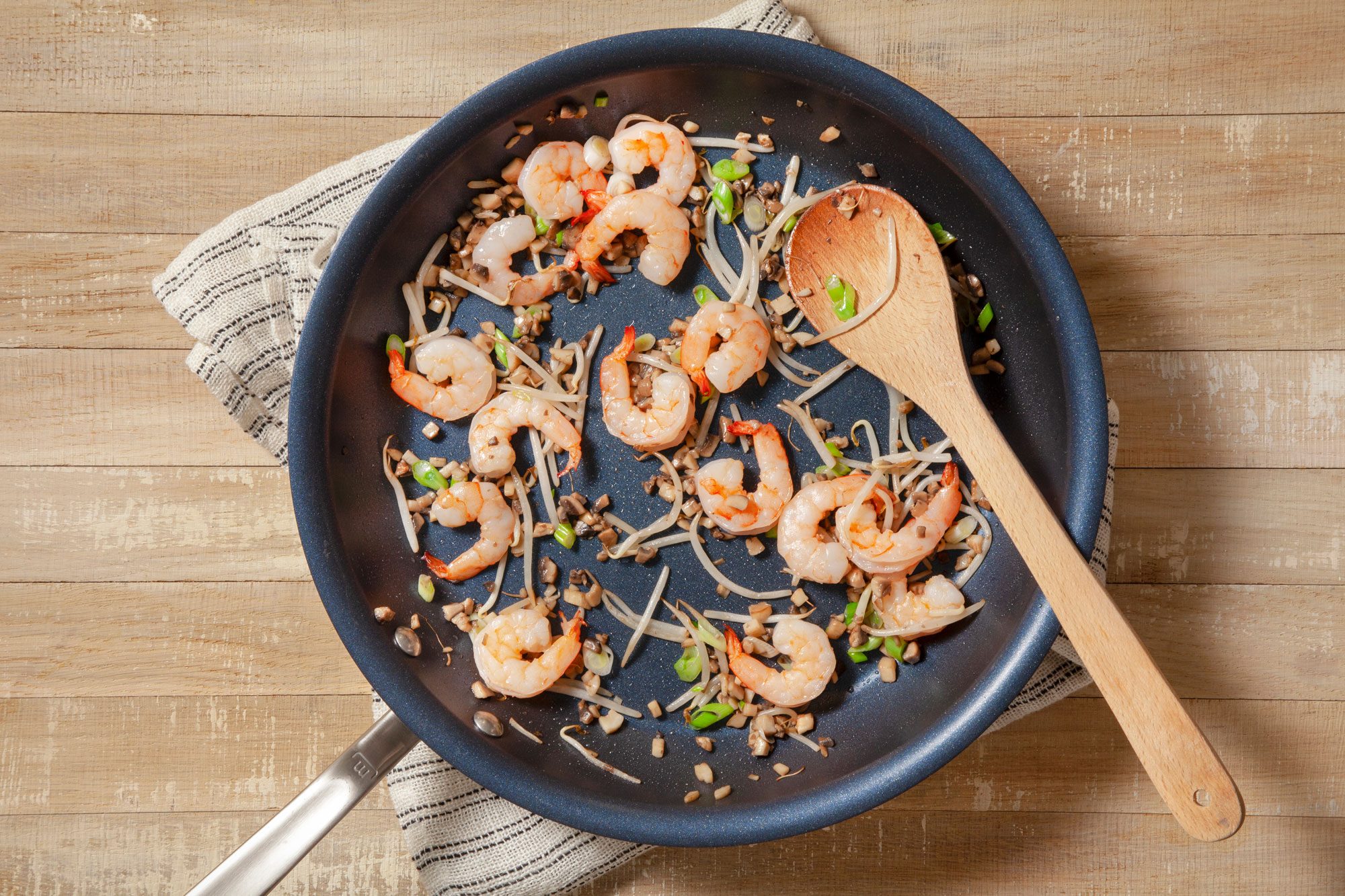 Sauteed Shrimps, Bean Sprouts and Onions with a Spatula in a Pan on Wooden Surface