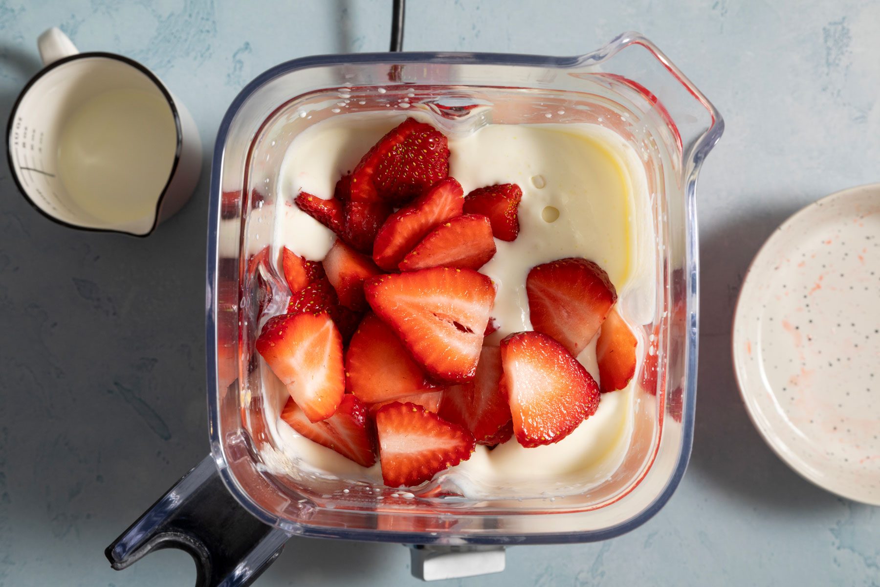 mixing strawberries into the blender on a marble countertop