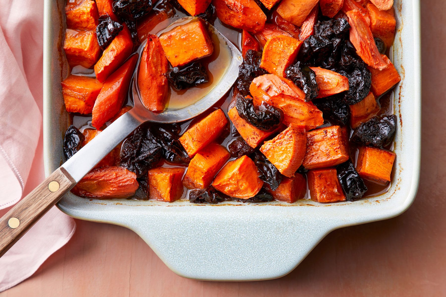 Tzimmes in a baking pan with a big spoon on a wooden surface
