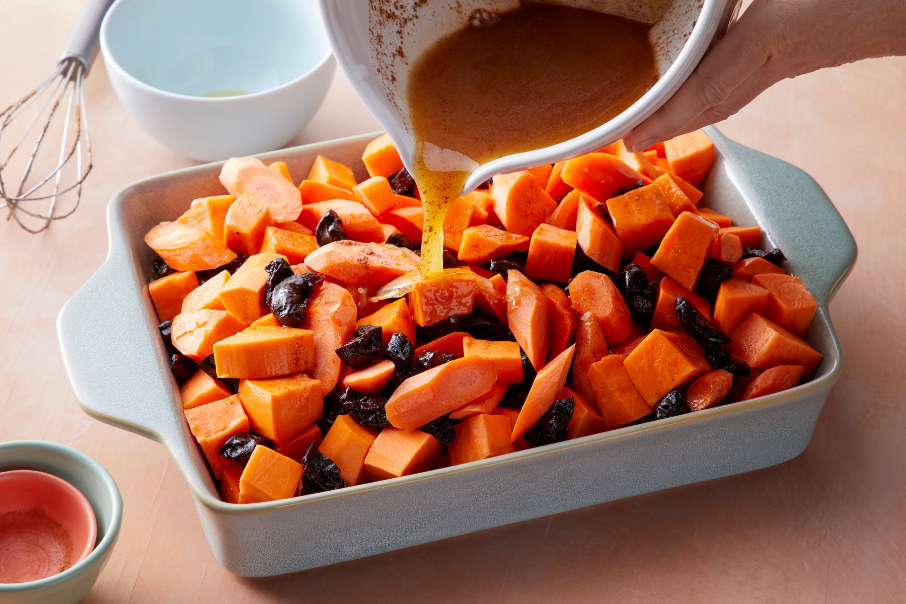 Pouring a mixture over vegetables on a large baking pan