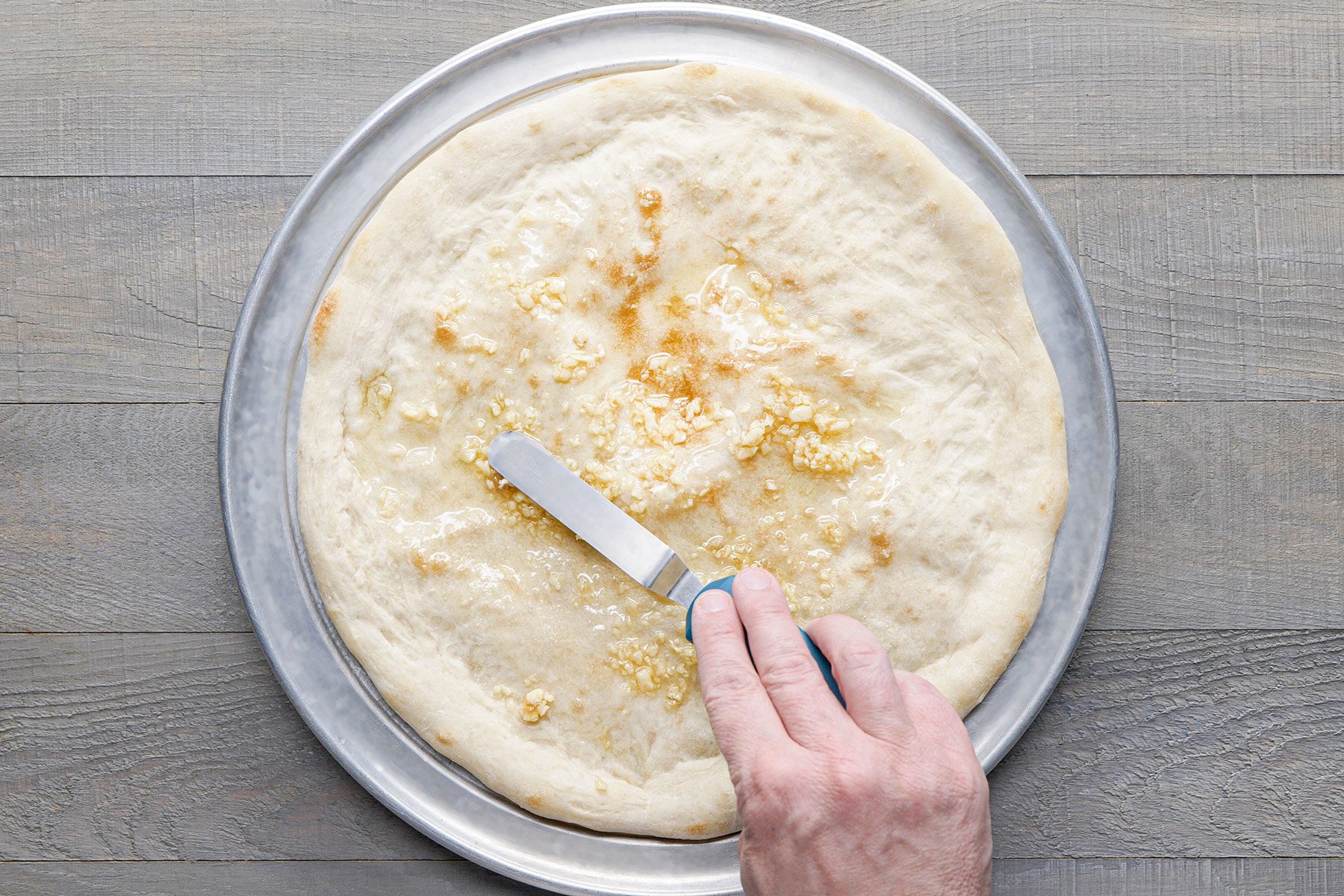 Spreading oil and garlic on pizza base