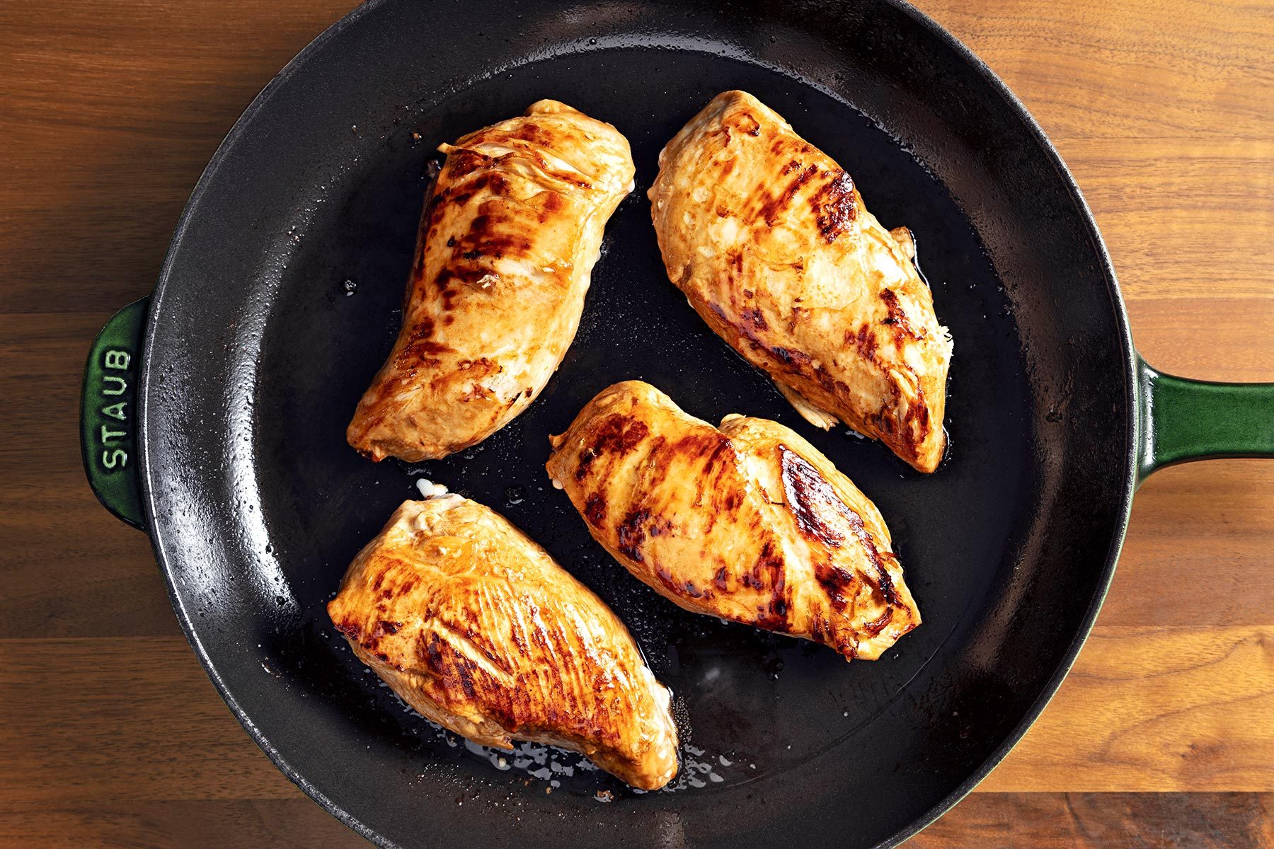 Overhead shot of cooked chicken breats; in a large overproof skillet; brown wooden background;