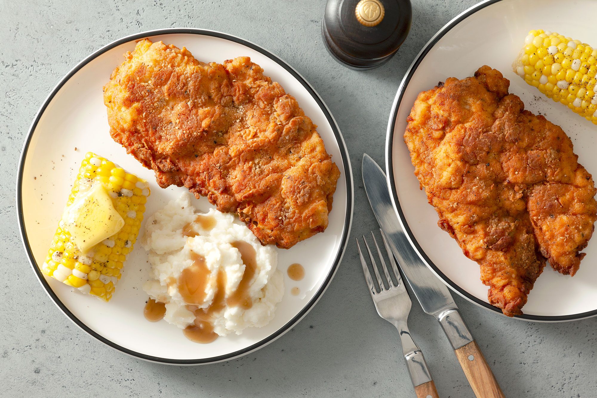 Crispy Fried Chicken Breasts Served with Boiled Corn on Two Small Plates on a Grey Surface