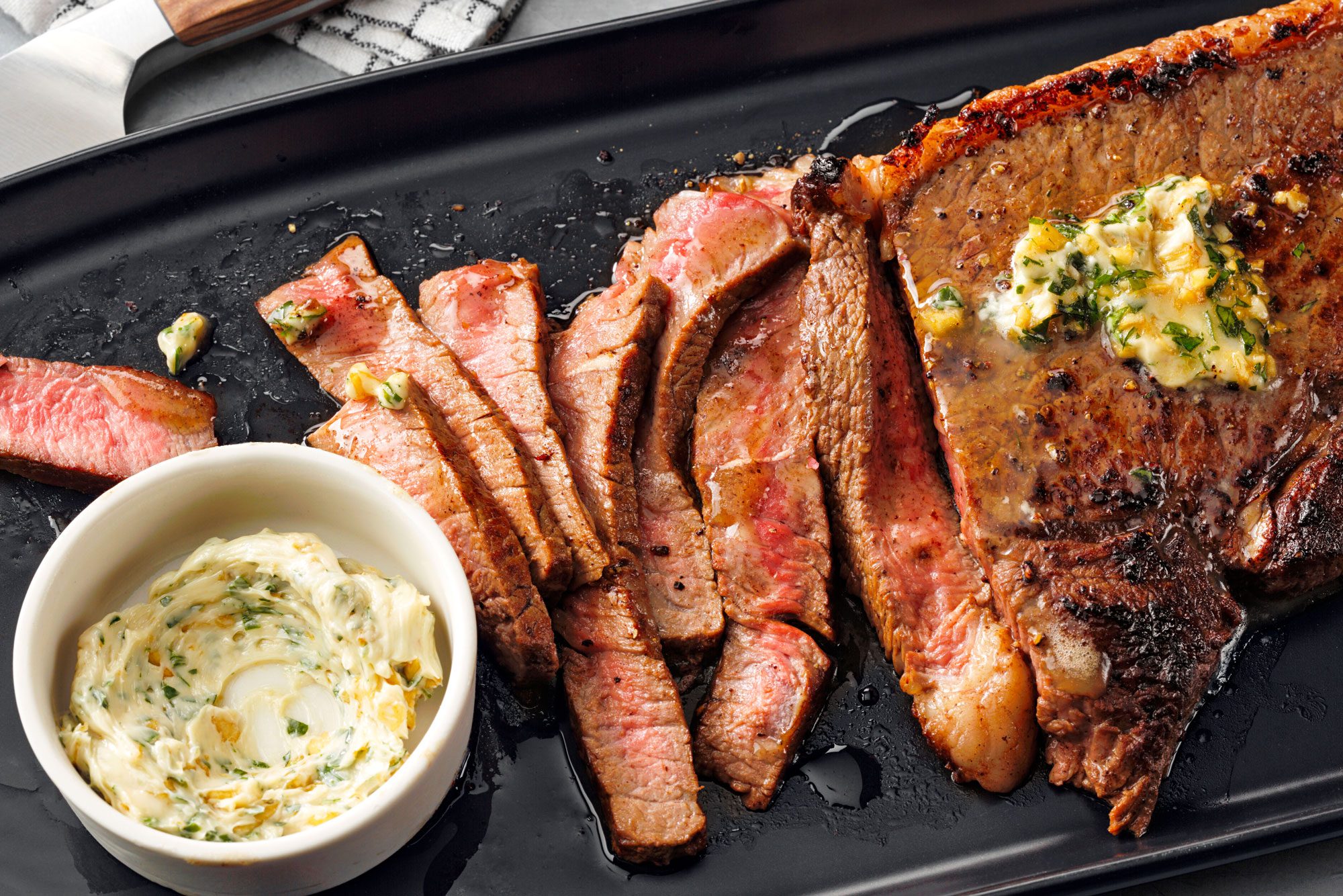 An appetizing garlic-butter steak placed on a black serving plate, garnished with butter
