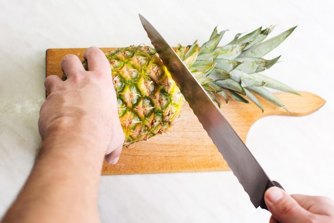 hand cutting the top off of a pineapple