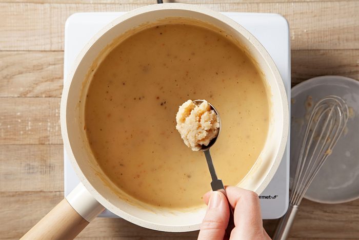 Overhead shot of a small saucepan; ham gravy; induction stove; whisk tool; wooden background;