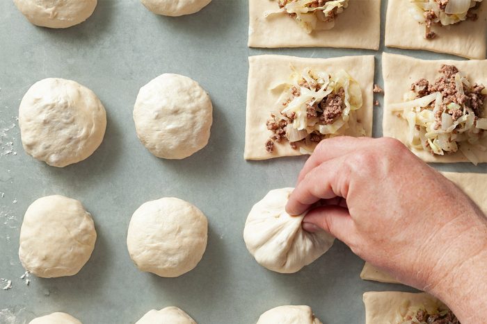 A hand is pinching a dough ball filled with a mixture of meat and chopped vegetables.