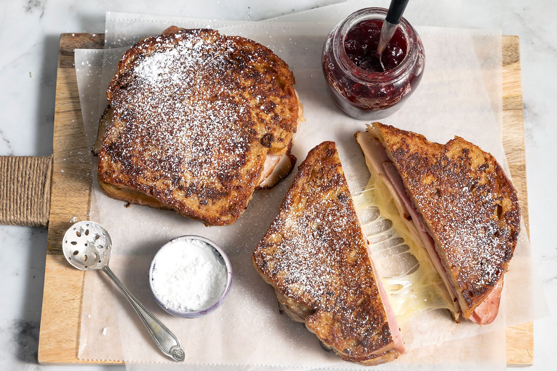 Monte Cristo Sandwich served on wooden board with jar of jam on the side