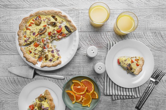 Quiche served on plate with orange juice and slices of oranges
