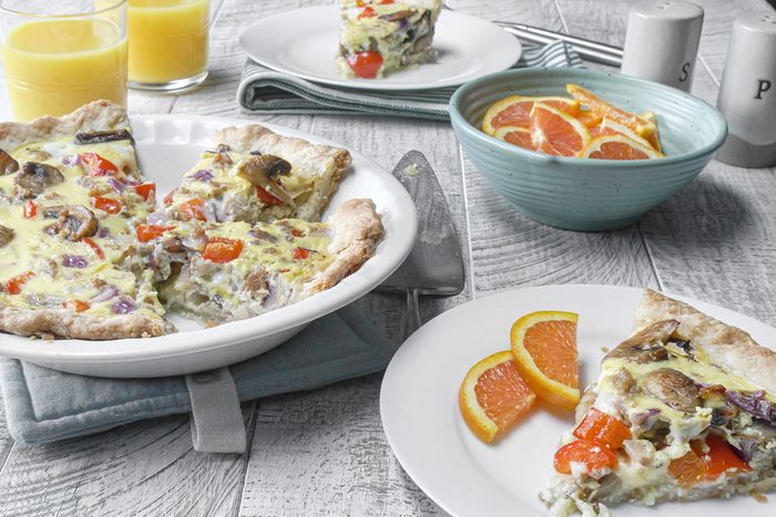 Quiche served on plate with orange juice and slices of oranges