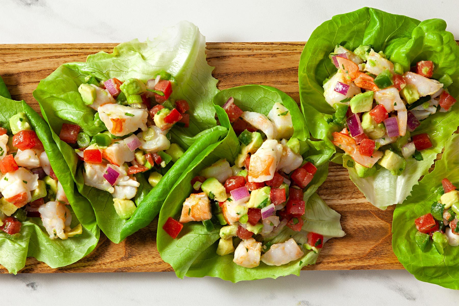 Overhead shot of Shrimp Avocado Salad; served in lettuce leaves; wooden tray; marble background;