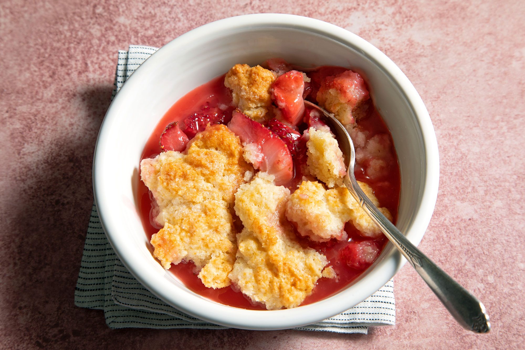 Strawberry Cobbler with Spoon in a White Bowl on a Pink Surface