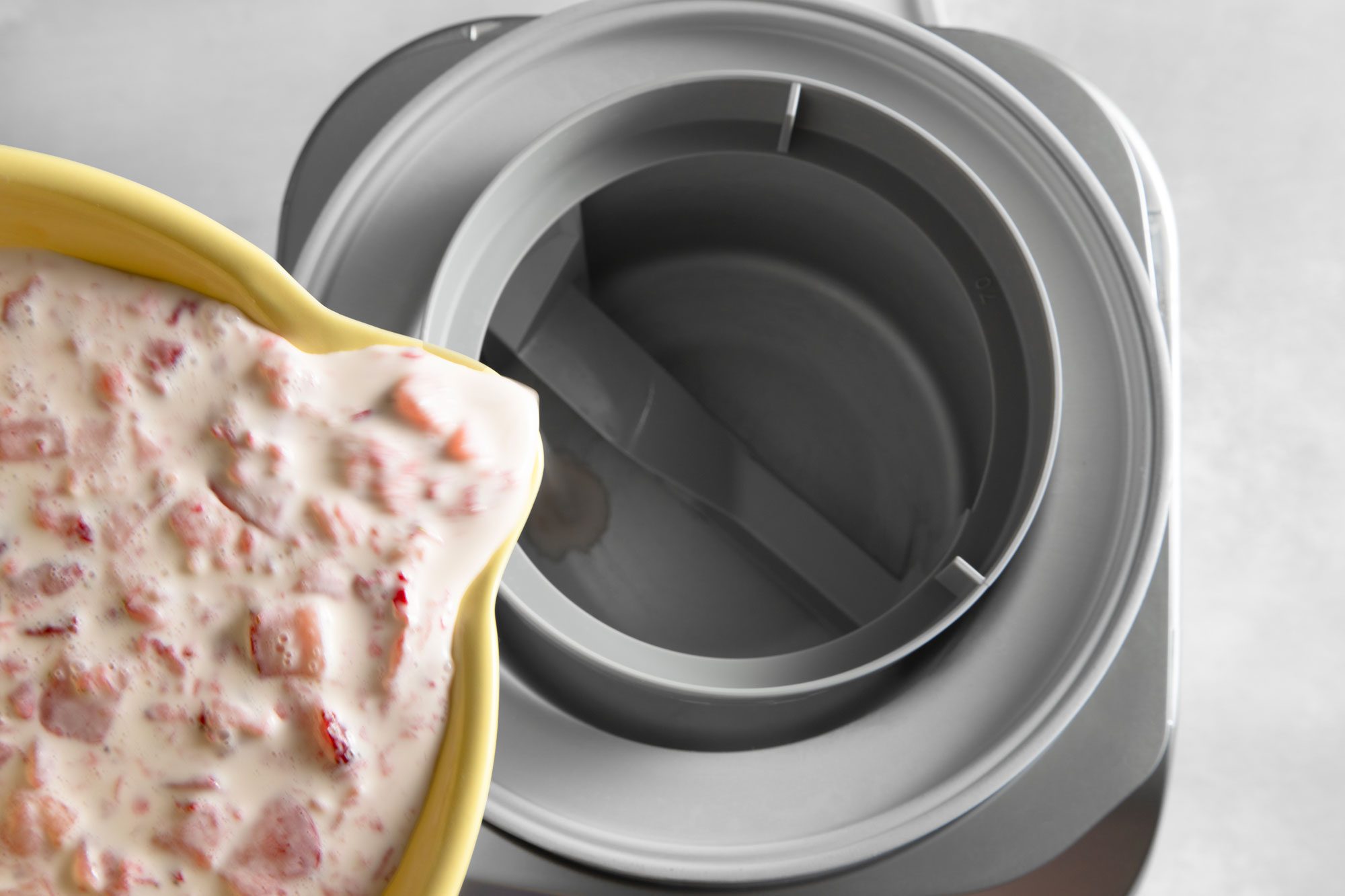 Overhead shot of transferring the Strawberry Ice Cream mixture to cylinder of ice cream maker on white marble background