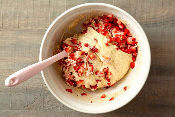 mixing strawberries with muffin batter in a large bowl on a wooden surface