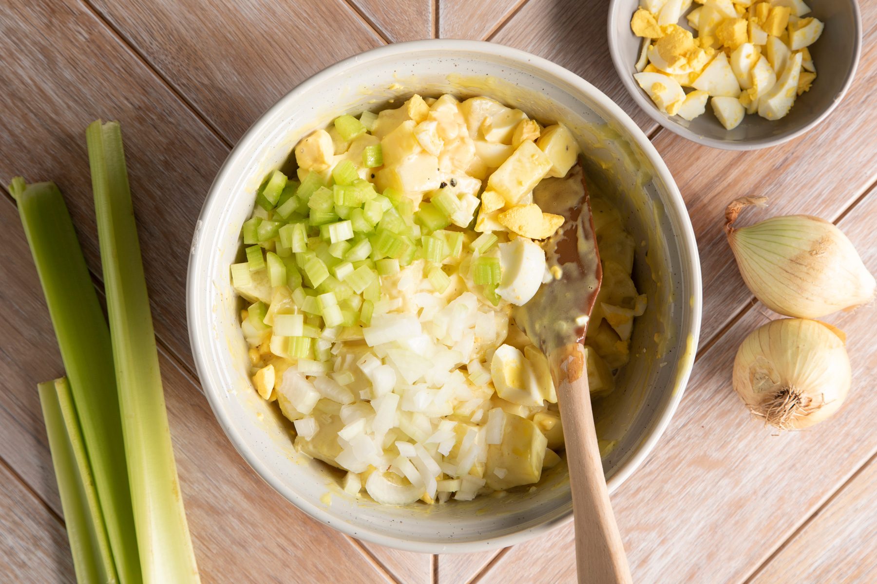 Eggs, onions, celery, and other ingredients being mixed with a spatula in a bowl