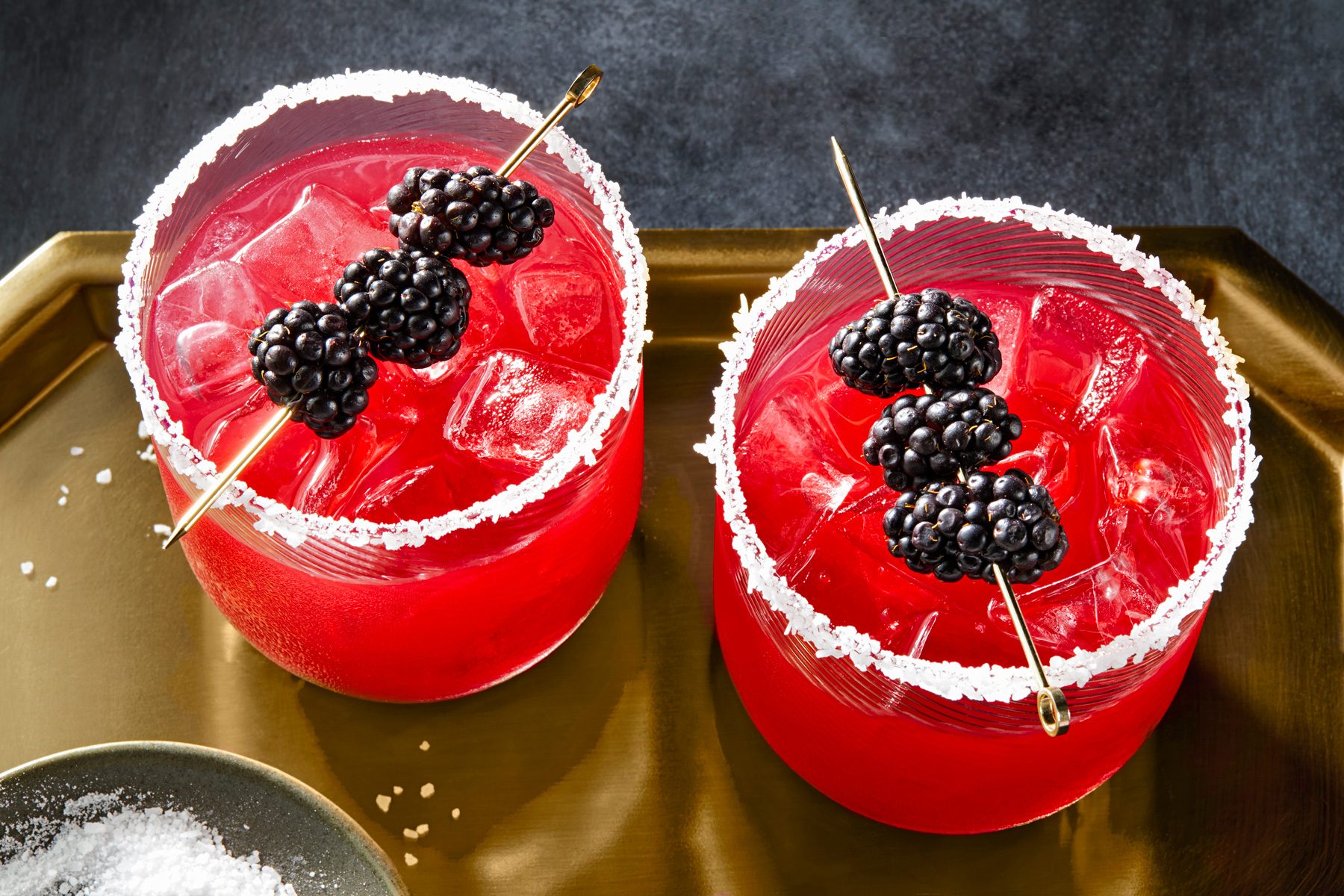 Two glasses of blackberry margarita with a salted rim, garnished with blackberries.