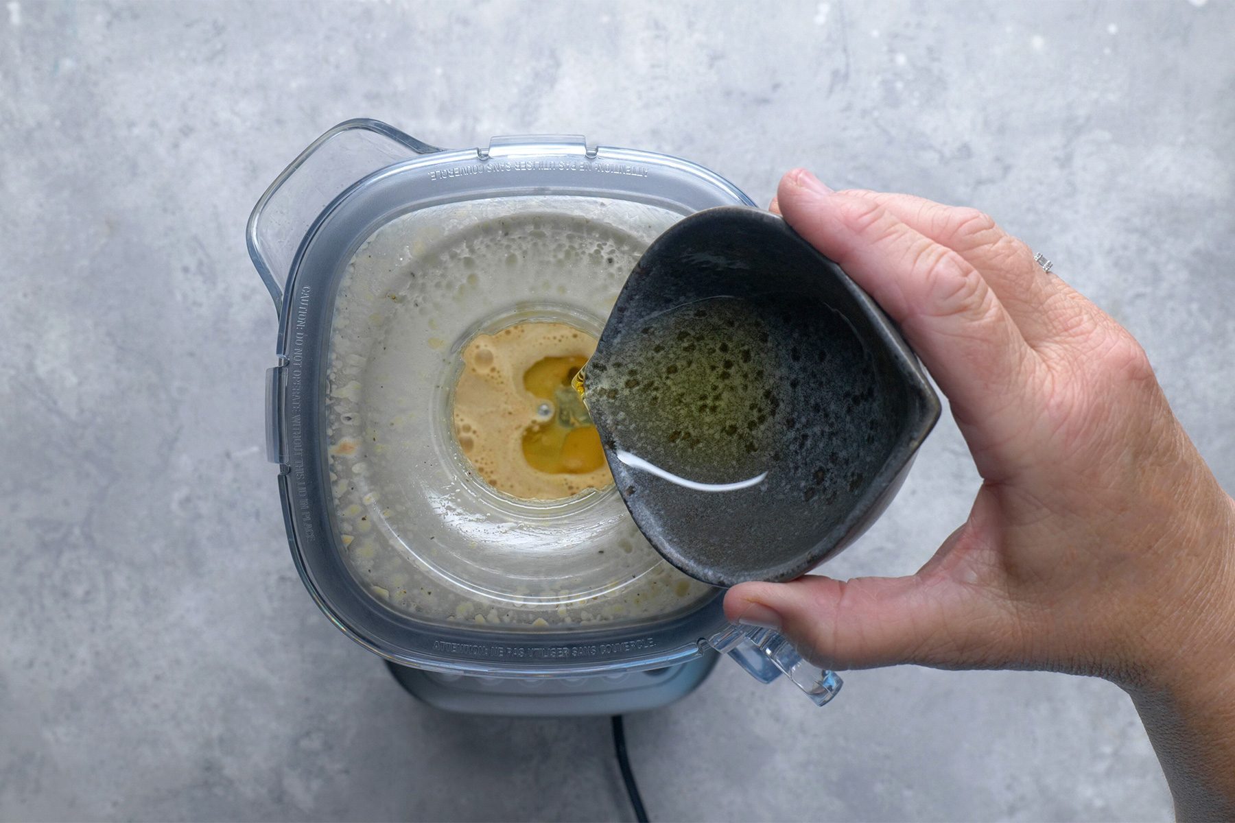 Overhead shot of add hot sauce; gradually add oil in a steady stream; grey background