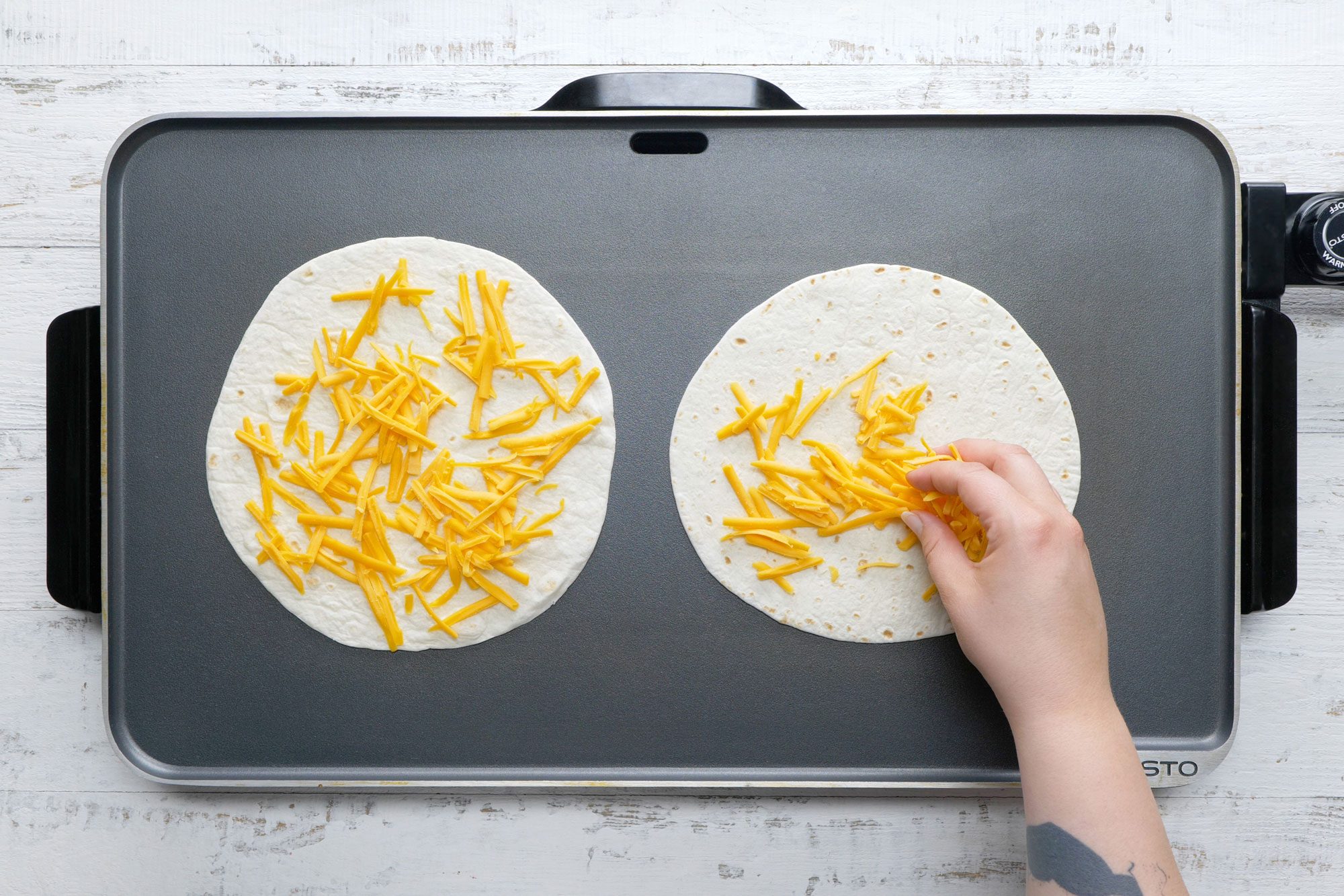 overhead shot of tortillas with cheese spreaded on top on a preheat griddle