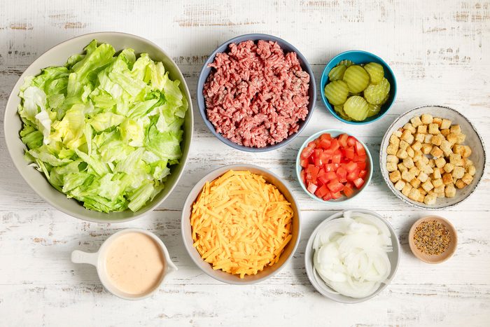 overhead shot; white textured background; Deluxe Cheeseburger Salad ingrediants;